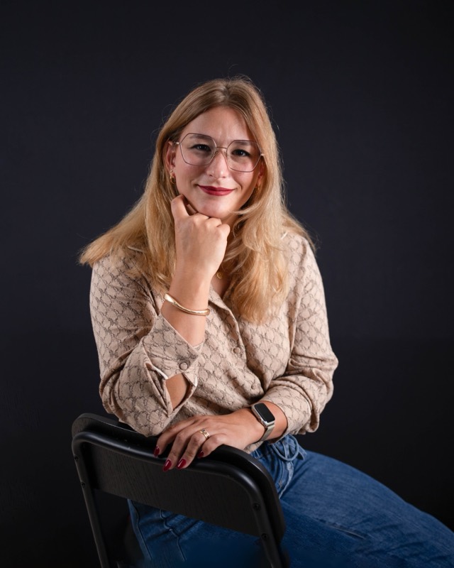 Laurine De Campos assise sur une chaise, le menton dans la main, souriante